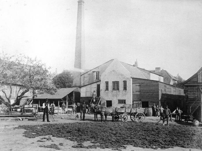 Fabrik. Skorsten. Hestevogne og arbejdsmænd.