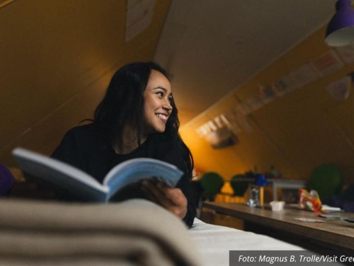 Young woman reading a book and smilling in a cottage in south greenland Photo by Magnus B Trolle - Visit Greenland