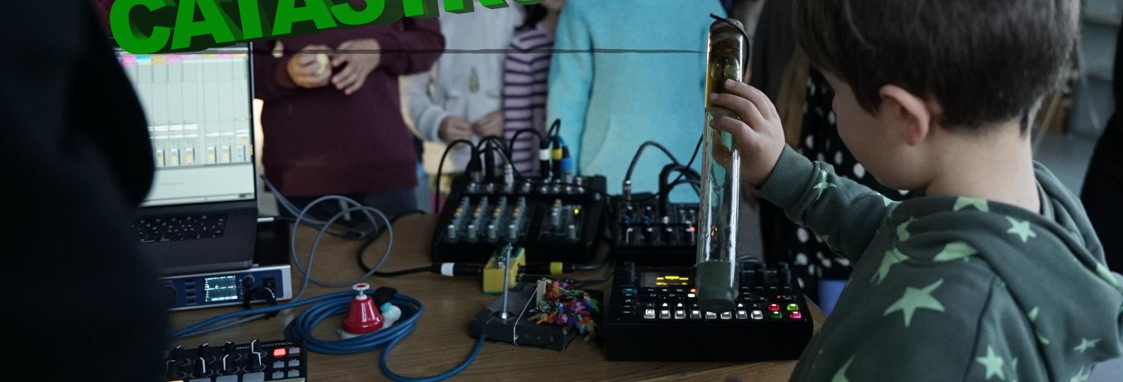 „Et barn fortolker regn med et hjemmelavet instrument, mens Mathias Loose manipulerer lydene med en loopstation. En skoleklasse lytter og kigger med i baggrunden.