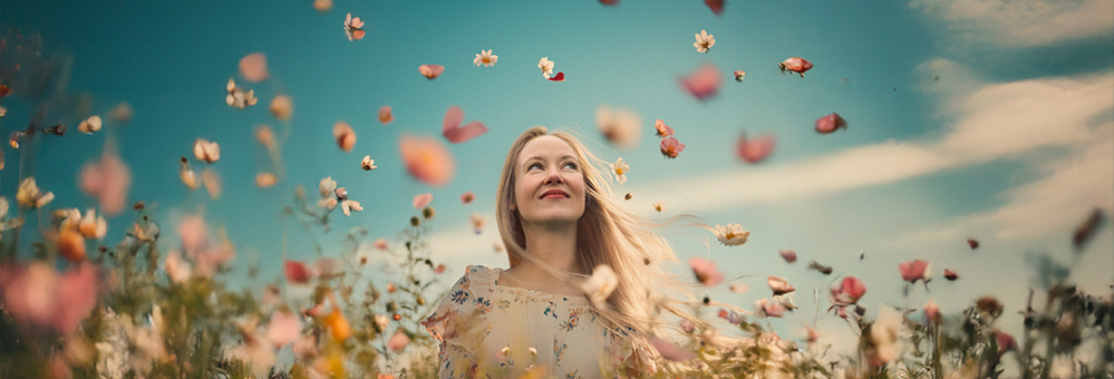 En glad pige står i en valmuemark med blomster, der flyver rundt i luften over hende
