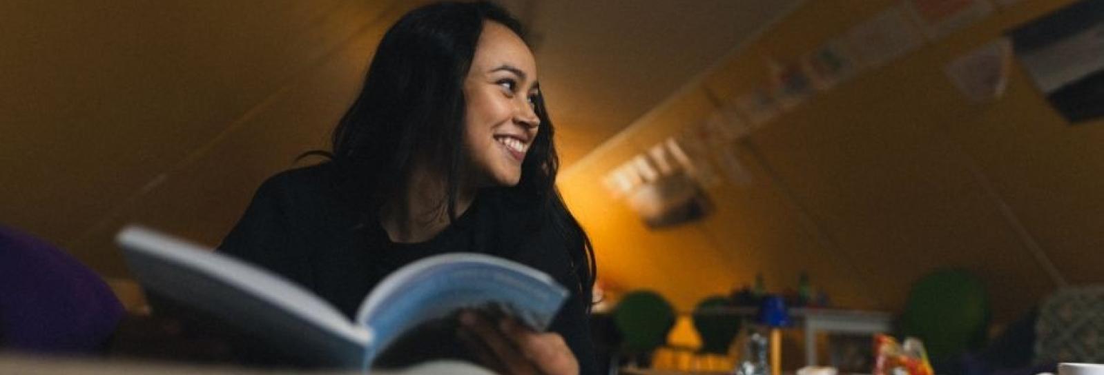 Young woman reading a book and smilling in a cottage in south greenland Photo by Magnus B Trolle - Visit Greenland