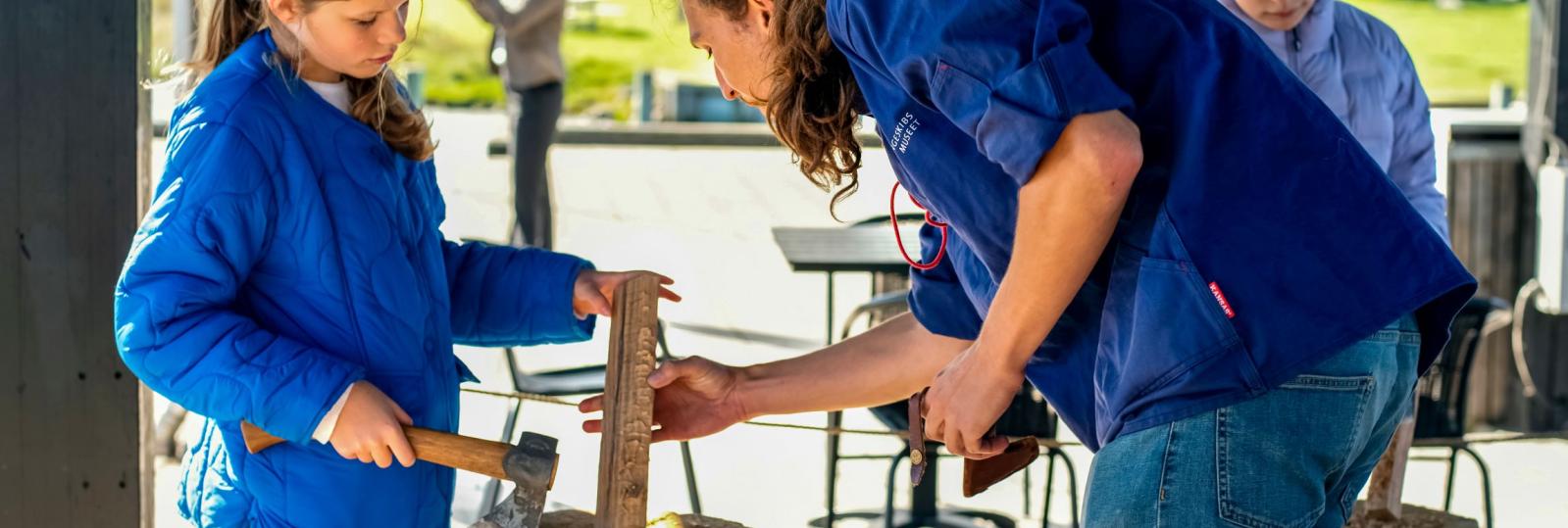 Underviser og elev arbejder med økse på træ til snelle