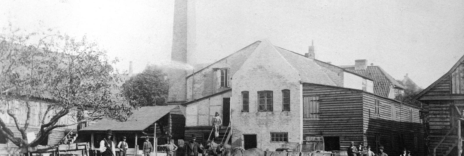 Fabrik. Skorsten. Hestevogne og arbejdsmænd.