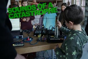 „Et barn fortolker regn med et hjemmelavet instrument, mens Mathias Loose manipulerer lydene med en loopstation. En skoleklasse lytter og kigger med i baggrunden.