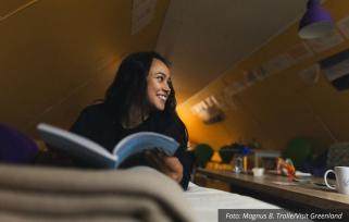Young woman reading a book and smilling in a cottage in south greenland Photo by Magnus B Trolle - Visit Greenland